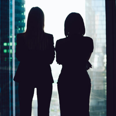 Colleagues standing near window looking at modern exterior of skyscrapers in business center