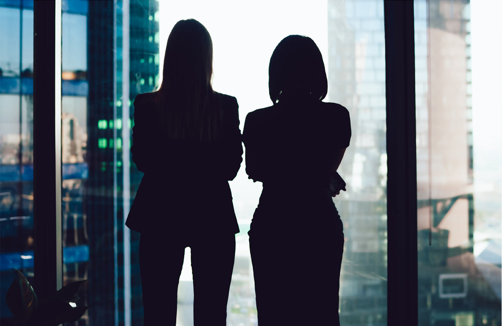 Colleagues standing near window looking at modern exterior of skyscrapers in business center